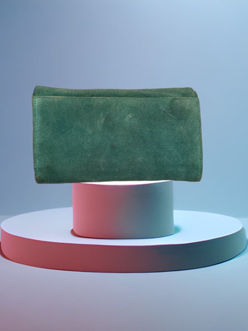 May include: A dark green suede clutch purse on a white and pink platform.