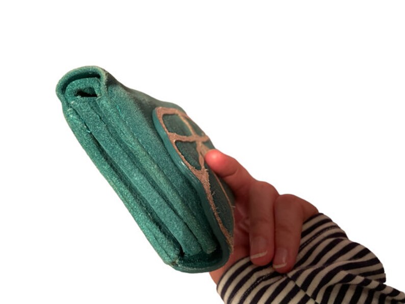 May include: A teal green leather wallet with a silver peace sign design.