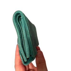May include: A teal blue leather wallet folded closed. The wallet is held in a hand.