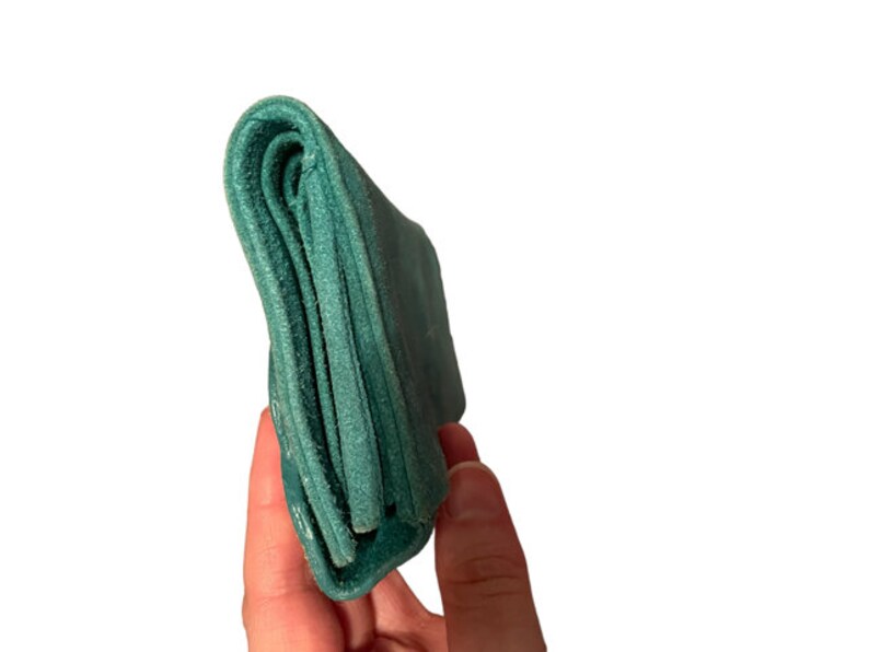 May include: A teal blue leather wallet folded closed. The wallet is held in a hand.
