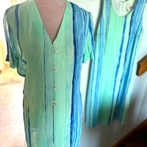 May include: Two dresses with vertical stripes in shades of blue and green. One is a button-down shirt dress with a V-neck and short sleeves. The other is a sleeveless dress hanging on a pink hanger.
