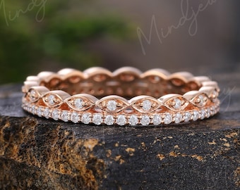 May include: Rose gold ring with two bands. The top band features a repeating pattern of small diamonds set in a delicate design. The bottom band is lined with a row of small, sparkling diamonds. The ring is displayed on a dark, textured surface.