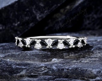 May include: A silver ring featuring alternating black and white gemstones. The ring's design includes marquise-cut black stones and round white stones, set in a continuous pattern. The ring is displayed on a dark, textured surface.