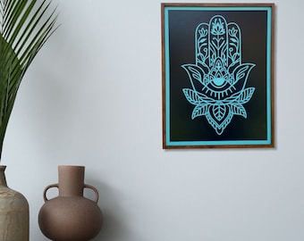 May include: A framed print of a hamsa hand with an eye in the center, outlined in turquoise blue on a black background. The frame is made of dark wood.