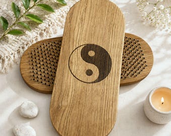 May include: Two oval wooden boards featuring a dark brown yin yang symbol engraved on the top surface. Each board is embedded with numerous small, evenly spaced metal nails protruding upwards, designed for standing or resting feet upon.