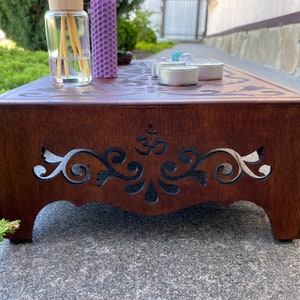 May include: A wooden altar with intricate cutouts and an Om symbol. The altar is brown and has a decorative design. There are candles and a diffuser on the altar.