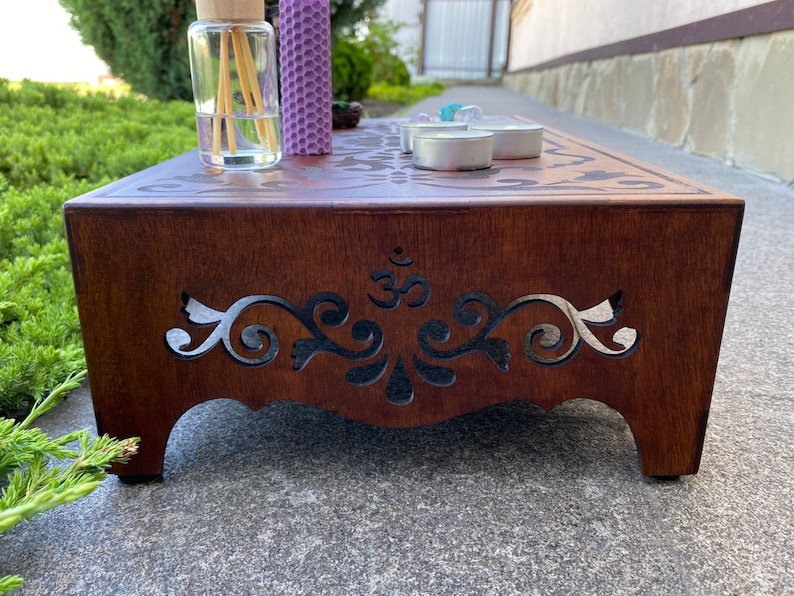 May include: A wooden altar with intricate cutouts and an Om symbol. The altar is brown and has a decorative design. There are candles and a diffuser on the altar.