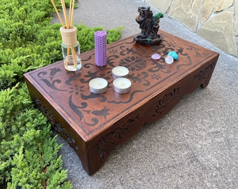 Puede incluir: Un altar de madera con intrincados tallados y un diseño floral. Cuenta con cuatro pequeñas velas blancas, dos piedras moradas y un pequeño árbol decorativo.