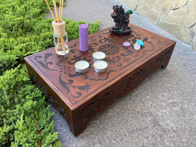 May include: A wooden altar with intricate carvings and a floral design. It features four small white candles, two purple stones, and a small decorative tree.
