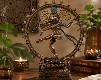 May include: A bronze-toned statue of Shiva Nataraja dancing within a circular ring of flames. The figure has multiple arms, wears a crown, and stands atop a small figure on a lotus base. The sculpture features intricate detailing and accents.