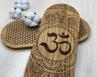May include: Two oval wooden boards featuring a bed of metal nails on one side and a laser-engraved Om symbol surrounded by intricate mandala patterns on the other. Three white cotton flower heads are placed on the nail bed surface.