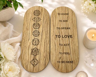 May include: Two oval wooden plaques with a light brown wood grain. The left plaque features seven vertically aligned chakra symbols. The right plaque displays the text: TO KNOW, TO SEE, TO SPEAK, TO LOVE, TO ACT, TO FEEL, TO BE HERE, engraved in black.
