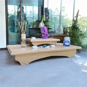 May include: Two tiered wooden shelves with a purple Ganesha statue, candles, and a glass jar with a blue label on the top shelf. The shelves are made of light wood with a natural grain.