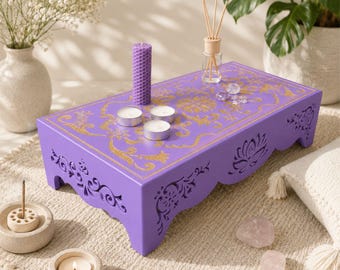 May include: A rectangular purple wooden meditation altar featuring intricate gold-colored floral patterns on the top surface and decorative cut-out designs on the sides. The altar holds a tall purple honeycomb candle and three small tea light candles.