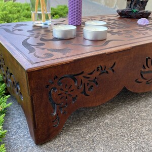 May include: A wooden altar with intricate carvings, featuring a lotus flower design. The altar is decorated with candles, incense sticks, and crystals.