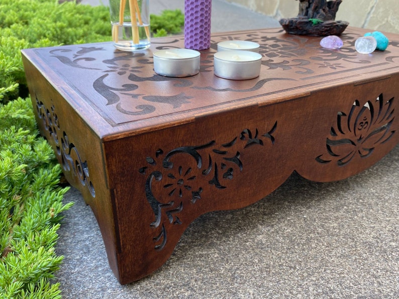 May include: A wooden altar with intricate carvings, featuring a lotus flower design. The altar is decorated with candles, incense sticks, and crystals.