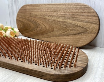 May include: A wooden oval-shaped board with a grid of small wooden pegs. The board is made of dark wood and the pegs are a lighter brown color. The board is designed for use as a sensory tool or for playing games.