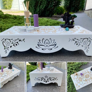 Op de afbeelding: Een witte houten meditatietafel met ingewikkelde uitgesneden ontwerpen en gouden accenten. De tafel heeft een lotusbloem en Om-symbool, met een decoratief patroon op het oppervlak. Het bevat kaarsen, wierook en een diffuser, waardoor een serene sfeer ontstaat.