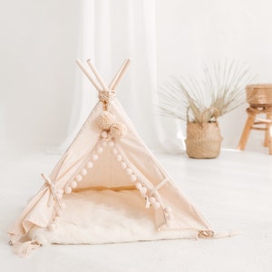 May include: A cream-colored teepee tent for children with a white faux fur mat and a white pom-pom trim.