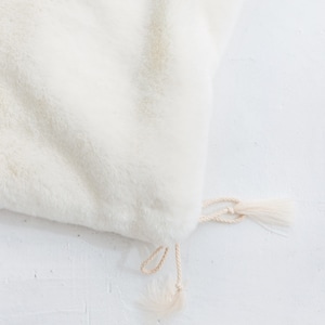 May include: A white faux fur pouch with a cream-colored drawstring and tassel.