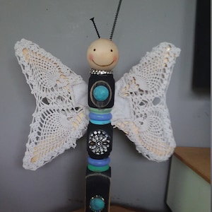 May include: A whimsical wooden butterfly figurine with white lace wings, a smiling face, and colorful beads and turquoise gems.