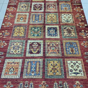 May include: A rectangular, red area rug with a repeating pattern of square panels. Each panel features a unique, intricate design in shades of gold, blue, green, and brown. The rug's border has a detailed floral pattern.