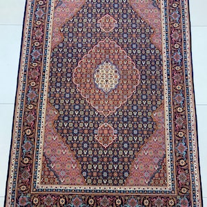 May include: Rectangular Persian rug with a navy blue field and intricate floral and geometric patterns in shades of red, pink, and cream. The rug features a central medallion design and a detailed border with fringe on the short ends.