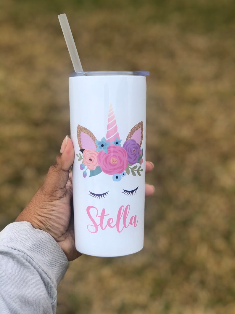 Peut inclure: Un gobelet en acier inoxydable blanc avec un motif de licorne orn&eacute; de fleurs roses, violettes et bleues, d'accents de paillettes dor&eacute;es et d'yeux ferm&eacute;s. Le nom "Stella" est &eacute;crit en rose sous la licorne.