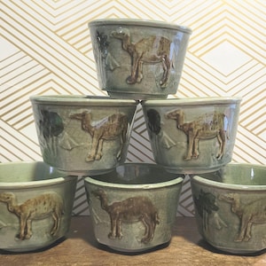 May include: A white ceramic mug with a black handle and the text "But First, Coffee" in a bold, black font. The mug is set against a blurred background, suggesting a cozy setting.