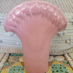 May include: A pink ceramic vase with a ruffled top, resembling a flower. The vase has a smooth, glossy finish.