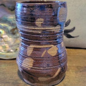 May include: A brown ceramic vase with a textured, striped design and a light brown glaze. The vase has a wide base and a narrow neck.