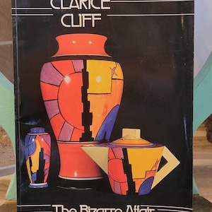 May include: A book cover titled Clarice Cliff The Bizarre Affair featuring a black background with illustrations of a large orange vase, a smaller purple and orange vase, and a yellow and orange teapot with geometric patterns and bold colors.
