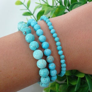 May include: Four turquoise beaded bracelets stacked on a person's wrist. The bracelets are made of round beads of varying sizes.