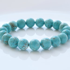 May include: Turquoise beaded bracelet with a light blue colour. The beads are round and have a smooth, polished finish.