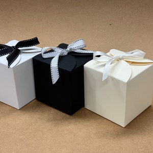 May include: Three gift boxes with different coloured ribbons. The boxes are white, black, and cream. The ribbons are black with white polka dots, white with black polka dots, and white.