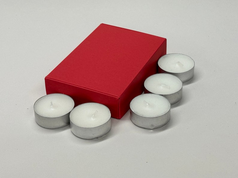 May include: A red box with six white tea light candles. The candles are in a silver holder.