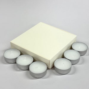 May include: A white square box with a set of eight silver tea light candles.