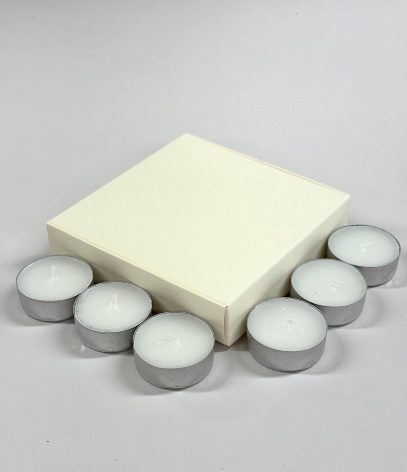May include: A white square box with a set of eight silver tea light candles.