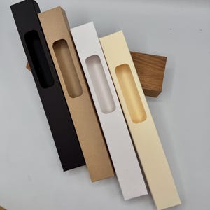 May include: Five cardboard boxes with a window cut out. The boxes are black, brown, white, and cream. The boxes are all the same size and shape.