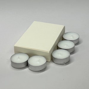 May include: A white box with six white tea light candles. The candles are in a silver holder.
