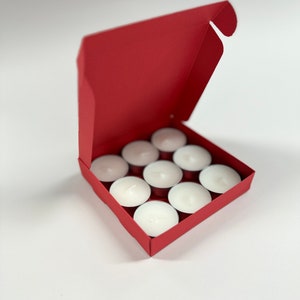 May include: A red cardboard box with the lid open, revealing a set of 10 white tea light candles.