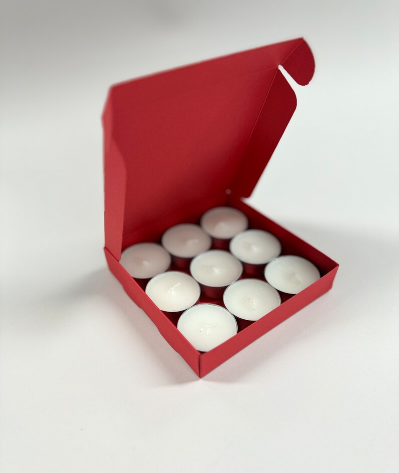 May include: A red cardboard box with the lid open, revealing a set of 10 white tea light candles.