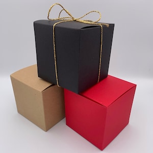 May include: Three gift boxes stacked on top of each other. The top box is black with a gold ribbon. The middle box is brown. The bottom box is red.