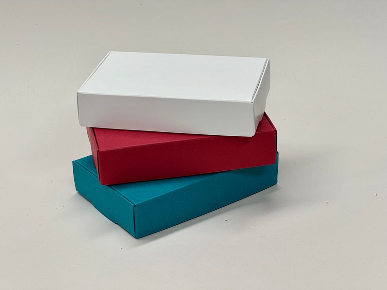 May include: Three boxes stacked on top of each other. The top box is white, the middle box is red, and the bottom box is teal.