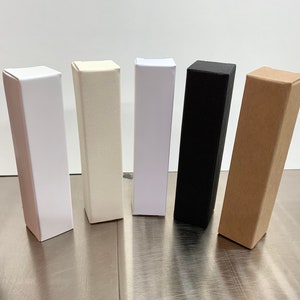 May include: Five cardboard boxes in different colours: white, off-white, black, and brown. The boxes are all the same size and shape, and they are arranged in a row from left to right.