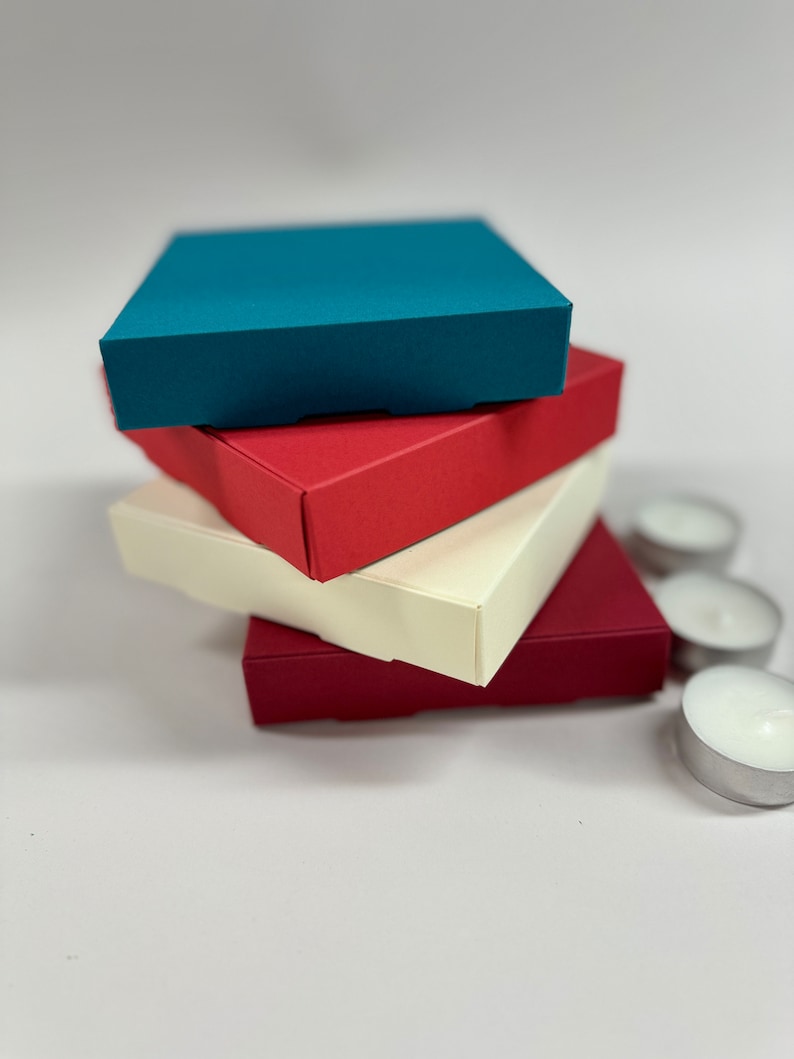 May include: Four square boxes stacked on top of each other. The top box is teal blue, the second box is red, the third box is cream, and the bottom box is burgundy.