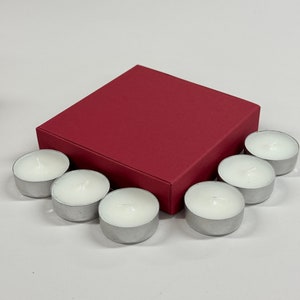 May include: A set of seven white tea lights in silver containers, arranged around a red square box.