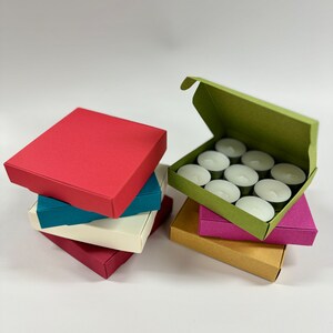 May include: A set of teal, red, white, pink, and brown boxes. The boxes are stacked on top of each other. The top box is red and the bottom box is brown. The boxes are filled with tea lights.