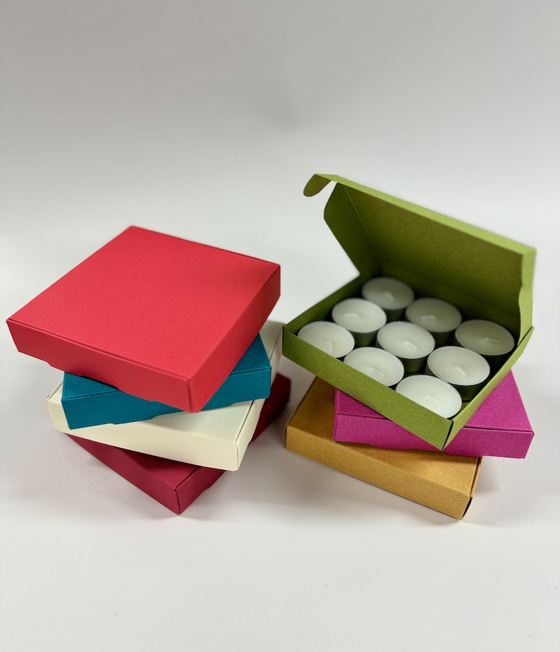 May include: A set of teal, red, white, pink, and brown boxes. The boxes are stacked on top of each other. The top box is red and the bottom box is brown. The boxes are filled with tea lights.