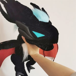 May include: Black plush dragon with blue and white fur accents. The dragon has red wings and a long tail.